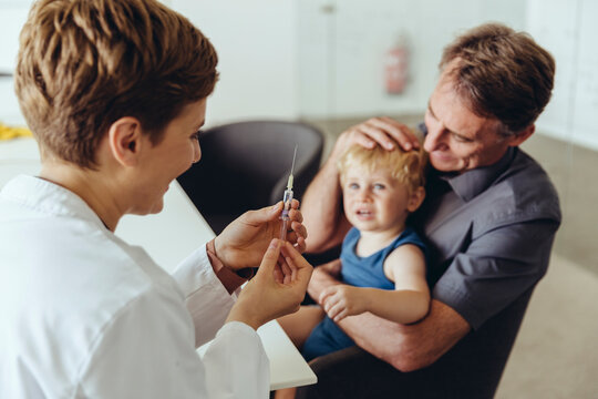 Father holding son while being vaccinated by pedeatrician