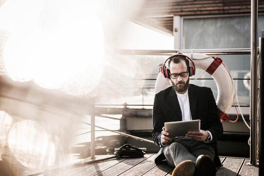 Hip businessman working on a houseboat, using headphones and digital tablet