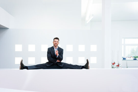 Smiling businessman doing the splits on reception desk in office