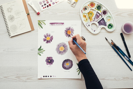 Woman painting flowers with water colors, top view