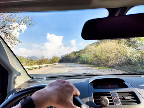 view through car windshield of natural landscape with green field, white clouds in blue sky. Hand of woman on steering wheel of car. Female traveler