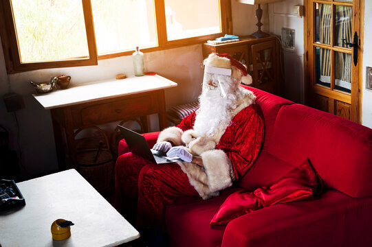 Man wearing Santa Claus costume using laptop while sitting on sofa at home