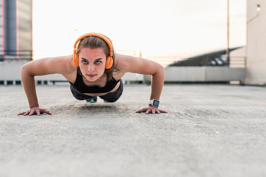 Woman with headphones doing pushups on parking level in the city