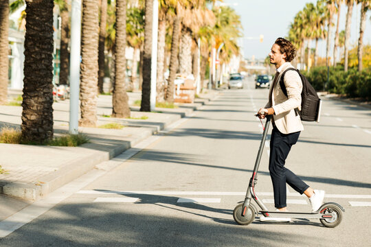 Man with backpack and E-Scooter crossing the street