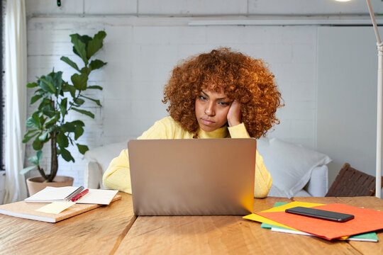 Bored businesswoman with hand in hair working on laptop at home