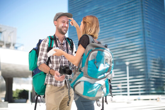 Woman with backpack applying suncream on boyfriend's face