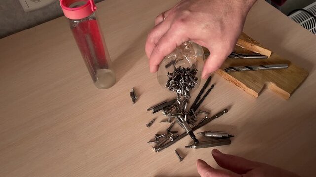 Metal screws spilling from plastic container onto wooden table closeup hardware fasteners scattered on work surface construction repair tools workshop concept DIY materials preparation and sorting