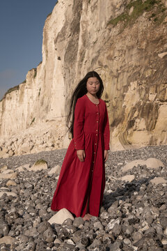 young woman in classic red dress beneath the cliffs of Normandy on the beach