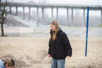 Happy Teenage Girl in Black Puffer Jacket Outdoors on a Cloudy Day near a Bridge © dizfoto1973