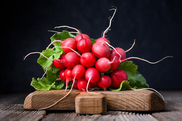Fresh red radishes with leafy tops on wooden board in low key lighting. Natural vegetables for...