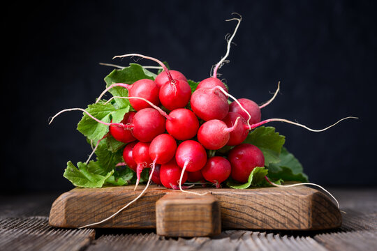 Fresh red radishes with leafy tops on wooden board in low key lighting. Natural vegetables for detox diet and rustic food styling