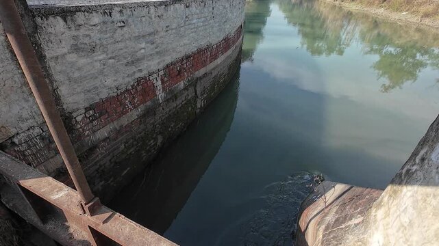 Wide-angle view of a rural irrigation canal with a small brick masonry check dam and rushing white water in a forested area of Haryana, India.