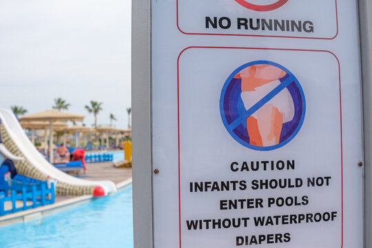 Warning sign at a swimming pool area indicating no running and caution for infants without waterproof diapers