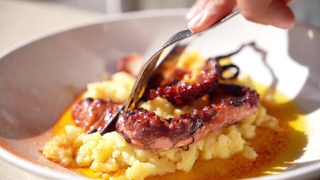 A person is eating a plate of food that has octopus on it. The plate is white and the food is orange