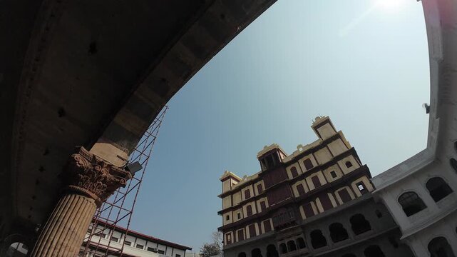 wide-angle perspective view of the historic Rajwada Palace courtyard in Indore, showcasing traditional stone arches and multi-storied galleries under a clear blue sky.