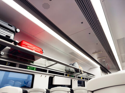 Inside a modern train car with overhead luggage and bright lighting, passengers seated and ready to travel