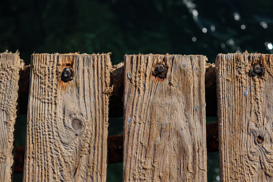 Close-up view of weathered wooden planks on a dock with visible nails and water reflections in the background