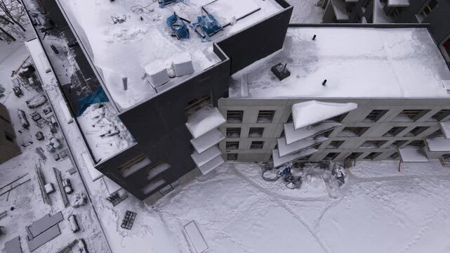 Aerial drone shot of a modern multi-story residential building under construction during winter. Overhead view highlighting urban development in cold weather conditions.