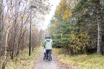 Obraz premium Parent walking with stroller and child on forest path in autumn