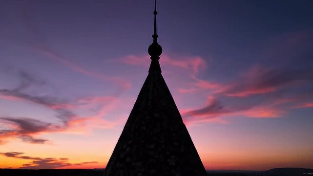 Silhouette of an ancient pyramid structure with a lit window against a dramatic twilight sky