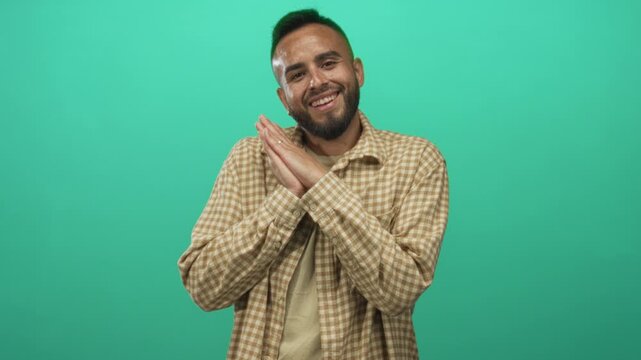 Man with hands clasped near chest and smiling face wearing checked shirt in a mint green studio; contentment.