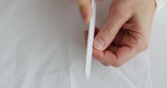 Female hands holding a nail file and giving herself a manicure on a white background