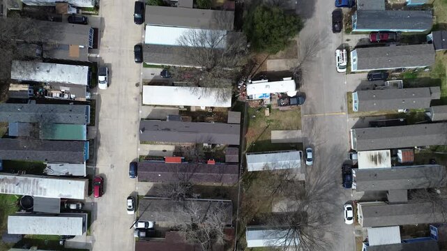 Long parallel rows of mobile homes sit within trailer park community near US 75 corridor, E Parker Rd. Mixed roof tone, scattered leafless trees, driveway vehicles, soft seasonal light, Plano, TX