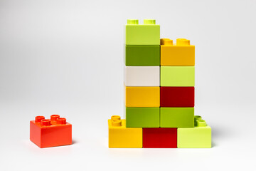 Fototapeta premium Colorful plastic building blocks stacked in a tower with a single red block placed separately on white background. Concept of teamwork, individuality, competition and business growth.