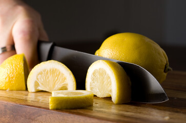 Man Cutting Lemon on Wood Cutting Board using a Black Knife