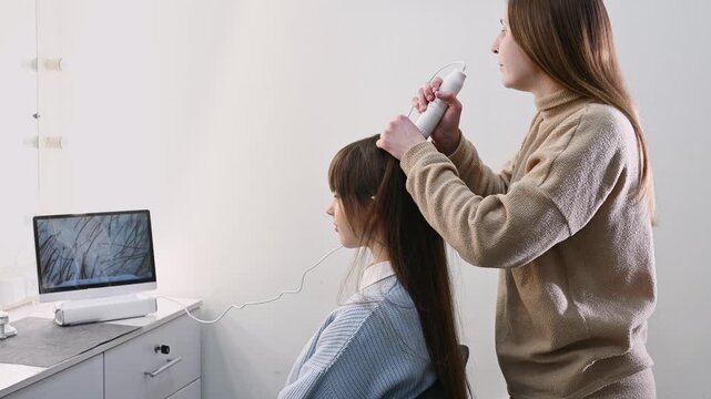 Trichologist examining scalp with digital dermatoscope, close up of hair and skin analysis on screen. Woman specialist performing hair diagnostics procedure in modern clinic, medical consultation conc