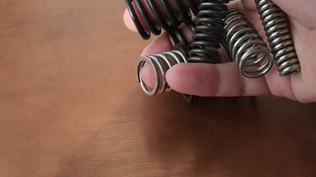 Metal springs of different sizes and materials in a hand. The spring on the ring finger simulates the movements of a mechanical hand. Copper surface.