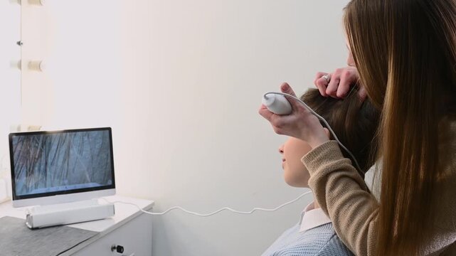 Trichologist examining scalp with digital dermatoscope, close up of hair and skin analysis on screen. Woman specialist performing hair diagnostics procedure in modern clinic, medical consultation conc