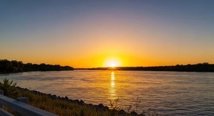 Fototapeta premium Riverside sunset with sun on water, dark trees, and sky gradient