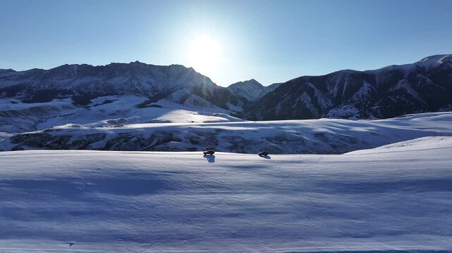 Two off-road cars driving through a vast snowy Dzungarian Alatau mountain landscape