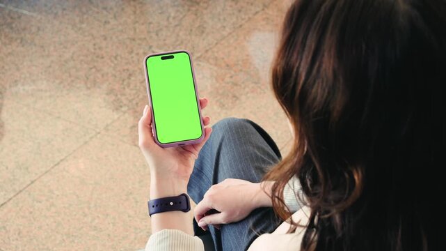 A woman sits in an airport terminal, using her phone, watching movies, reading the news, spending time on social media while waiting her flight. Phone with a green screen. High quality 4k footage