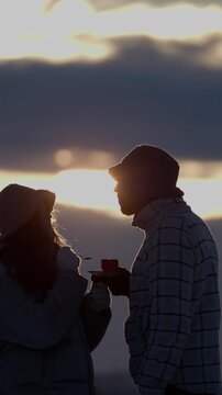 Silhouette of young wife feeds husband with cake at winter back sunset vertical video. Happy romantic couple celebrates Valentine day on active vacation in cold twilight nature