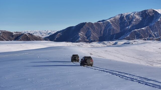 Aerial shot of two suvs driving through a vast snowy Dzungarian Alatau mountain landscape