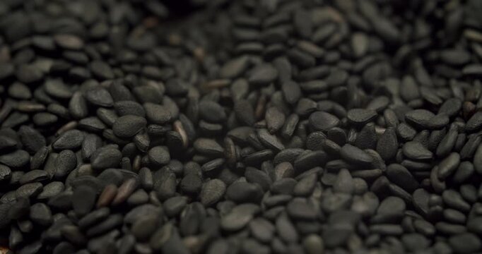 Super slow motion shot of black sesame seeds filling a wooden bowl isolated on a white background, Slow motion footage of a small wooden bowl full of black sesame seeds rotating on a white background