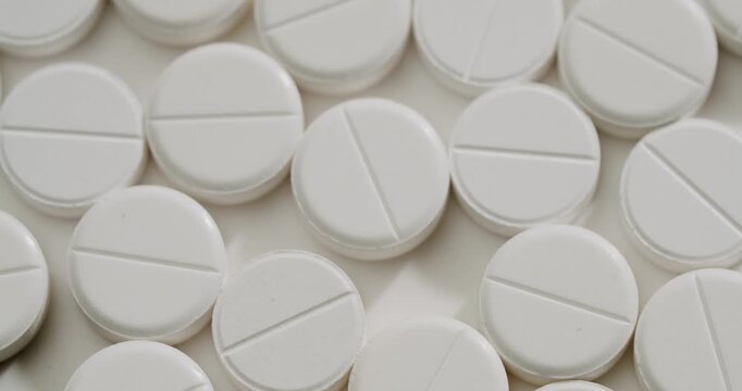 Macro view of many white round scored medical tablets slowly rotating on a clean surface, healthcare, and treatment for various diseases or addictions. White round medical pills rotating