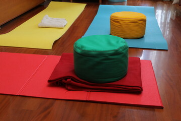 Colorful yoga mats and zafu meditation cushions on wooden floor