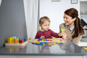 Preschool teacher laughing and helping a happy little girl learning shapes and colors with...