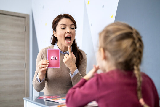 Speech therapist working with child, helping improve articulation and pronunciation using alphabet flashcards, focusing on speech development and communication skills