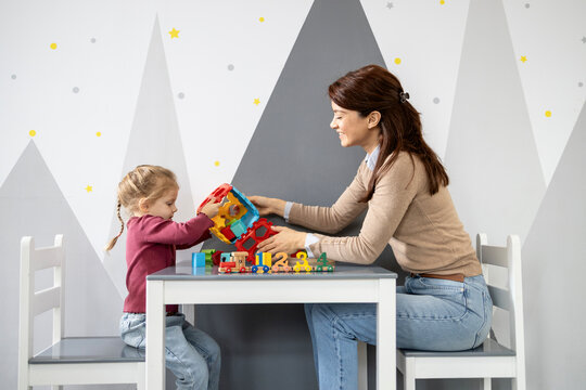 Preschool teacher interacting with a young girl, playing with educational toys at a small table, fostering early learning and development in a preschool classroom