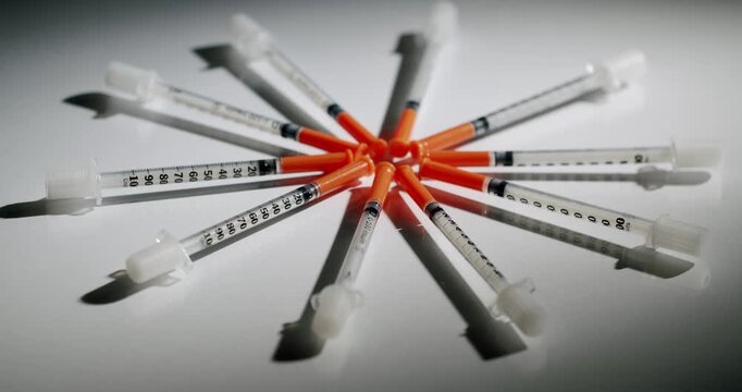 Large quantity of disposable insulin syringes with orange caps lying in a pile, slowly rotating on a clean white background, highlighting the concept of diabetes management and healthcare