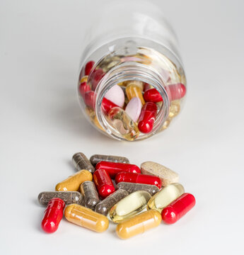 Various colorful capsules and dietary supplements in an open plastic bottle isolated on white background. Concept of medication, supplement culture, health trends, overuse and addiction, medical and s