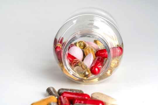 Various colorful capsules and dietary supplements in an open plastic bottle isolated on white background. Concept of medication, supplement culture, health trends, overuse and addiction, medical and s