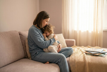 Mother Comforting Sick Child Sitting on Sofa at Home