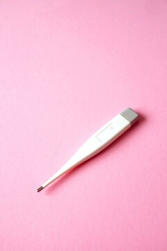 A white digital thermometer lies on a bright pink background with ample empty negative space. A minimalist composition focusing on healthcare and medical equipment. vertical