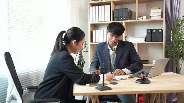 Two lawyers discuss legal documents at a desk, with a scale of justice and gavel symbolizing law, authority, and professional legal consultation in a modern office.