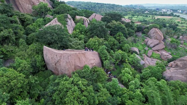 A cinematic aerial view of adventurers rappelling down a massive rock amidst the Ramanagara Hills